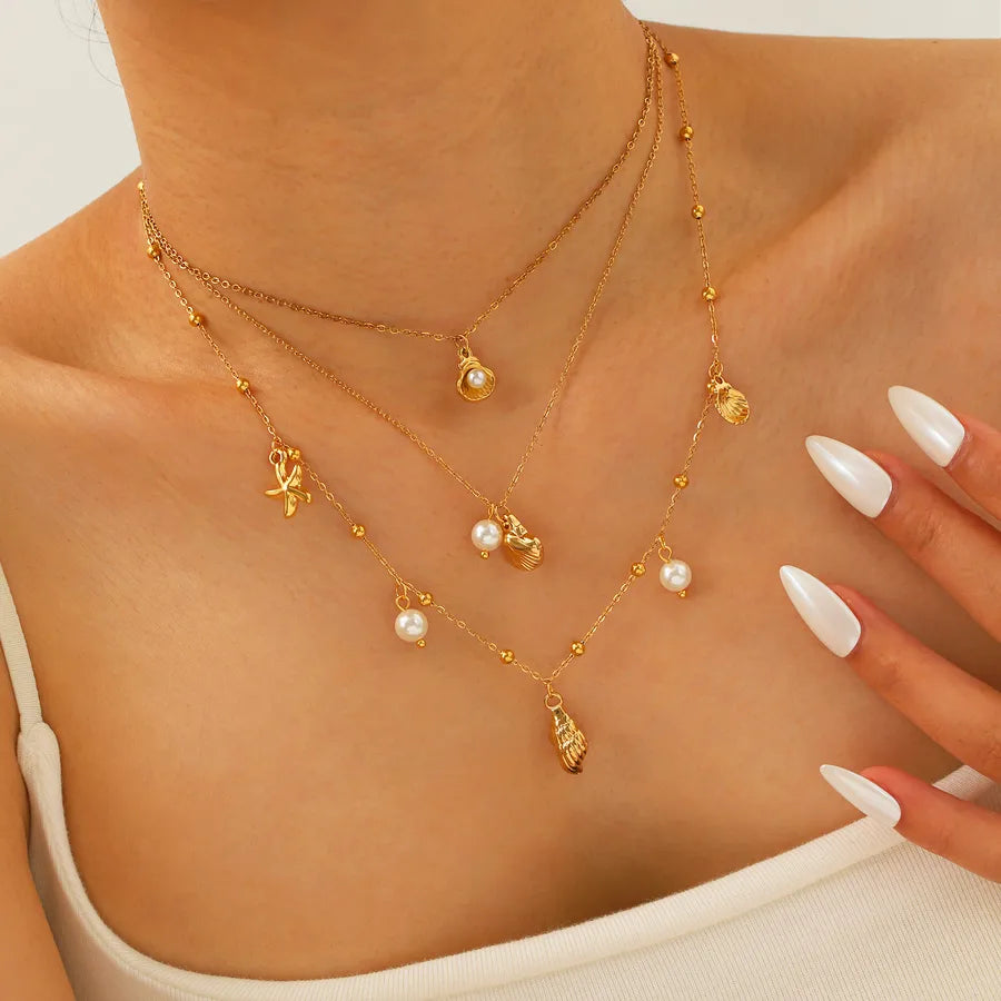 Gold necklaces with heart and star pendants on a person wearing a beige top.