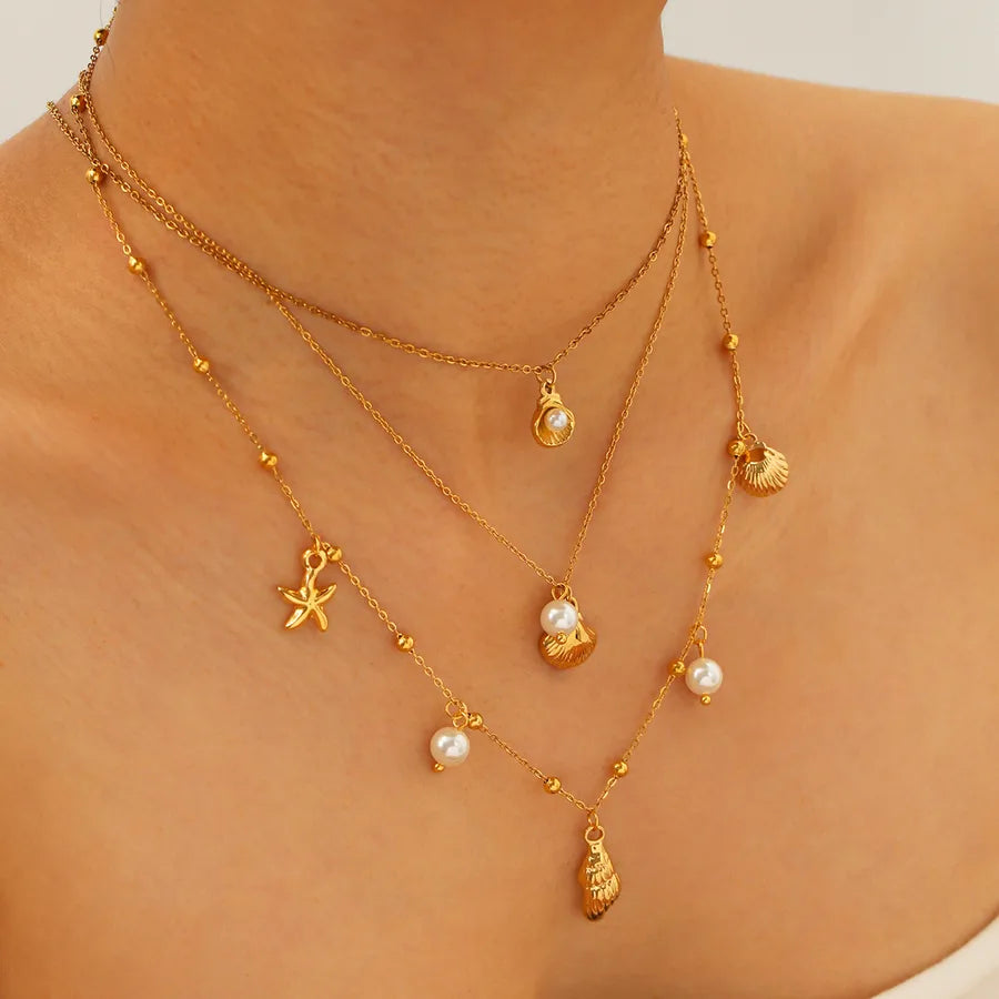 Gold necklaces with heart and star pendants on a person wearing a beige top.